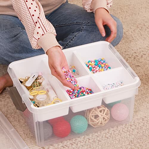 Person organizing colorful beads in a plastic storage box with compartments.