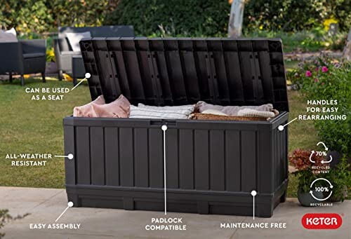 Keter outdoor storage box with open lid showing cushions inside, labeled features include seating function, all-weather resistance, easy assembly, padlock compatibility, maintenance-free, and recyclable content.