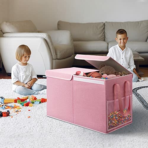 Two children playing with toys next to a large pink storage box in a living room.